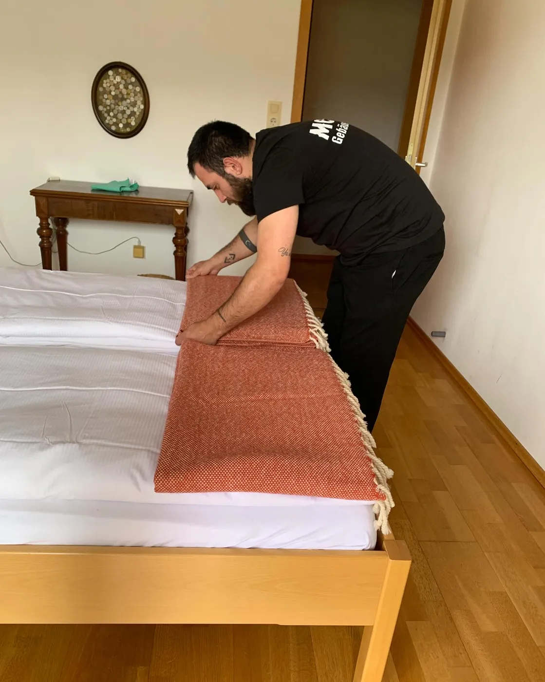 Mitarbeiter von Modus legt eine Tagesdecke auf ein frisch bezogenes Bett in einer Ferienwohnung
